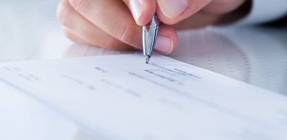 a person holding a pen over a piece of paper.