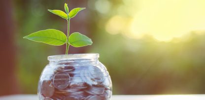 a glass jar filled with coins and a plant growing out of it.