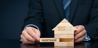 a man in a suit holding a wooden block with a house on it.