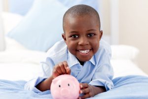 a young boy smiles while holding a pink piggy bank.