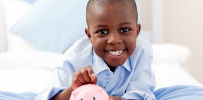a young boy smiles while holding a pink piggy bank.