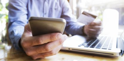 a man holding a credit card while using a laptop.