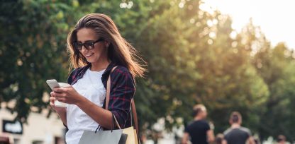 a woman holding shopping bags and looking at her cell phone.