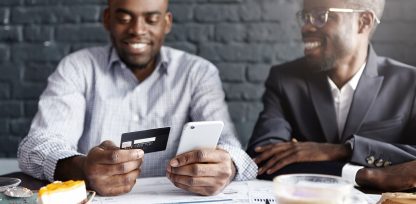 two men sitting at a table looking at a cell phone.