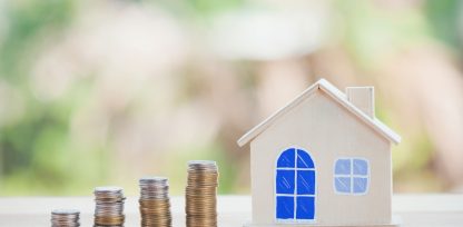 a small house sitting on top of a pile of coins.