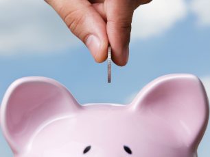 a person putting a coin into a pink piggy bank.